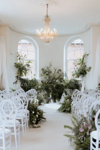 Light-filled ceremony setup at Iscoyd Park in Shropshire featuring white chairs, floral aisle arrangements and elegant chandelier décor, photographed by Cleo Stella Photography.