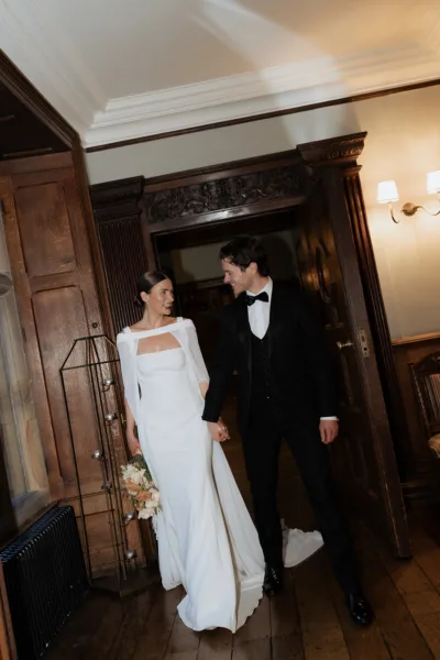 Bride and groom walking hand in hand through the historic doorway at Soughton Hall in Cheshire, captured in an editorial wedding photography style by Cleo Stella Photography.