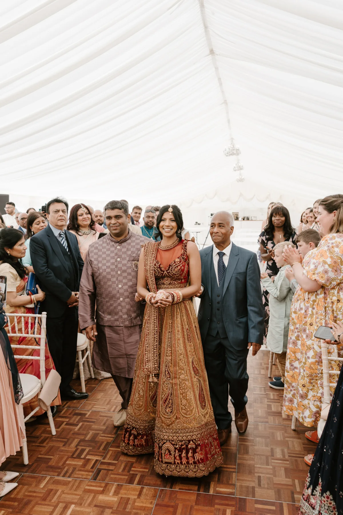 Fusion HIndu Wedding Newburgh Priory 19 - Hema & Will's Fusion Wedding & Hindu Ceremony at Newburgh Priory Hindu bride wearing a red and gold lehenga is accompanied down the aisle by her male family members.