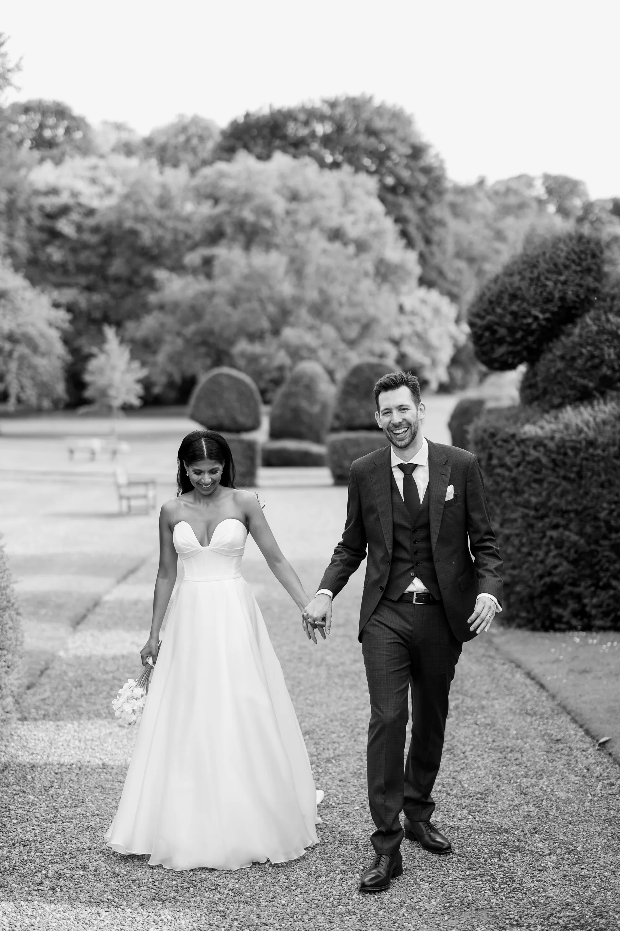 Fusion HIndu Wedding Newburgh Priory 73 - Hema & Will's Fusion Wedding & Hindu Ceremony at Newburgh Priory Black and white shot of a bride in a Suzanne Neville gown as she walks the grounds of Newburgh Priory hand in hand with her groom.