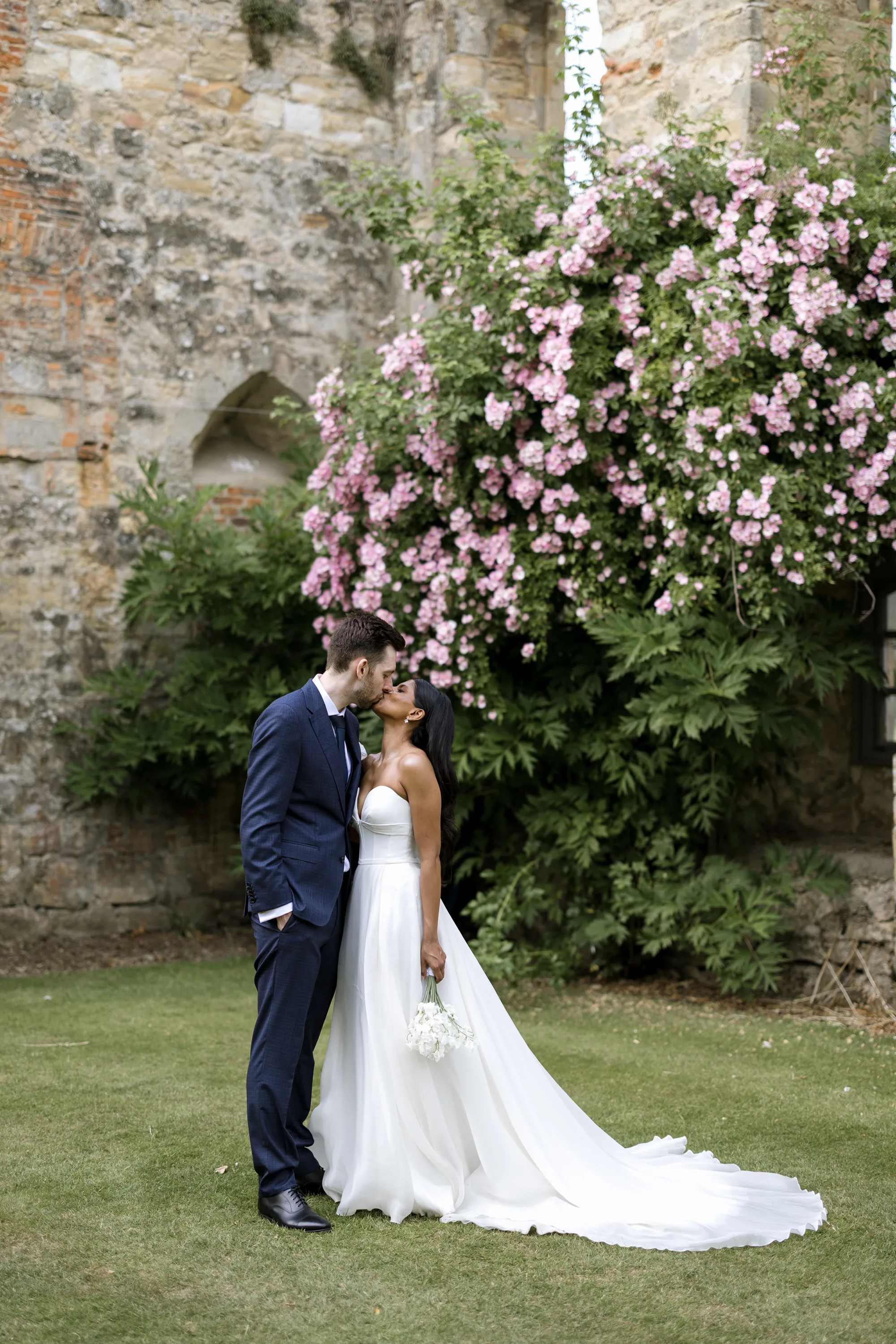 Fusion HIndu Wedding Newburgh Priory 75 - Hema & Will's Fusion Wedding & Hindu Ceremony at Newburgh Priory Bride and groom kissing in the grounds of Newburgh Priory, a pink Rhododendron bush in the background.
