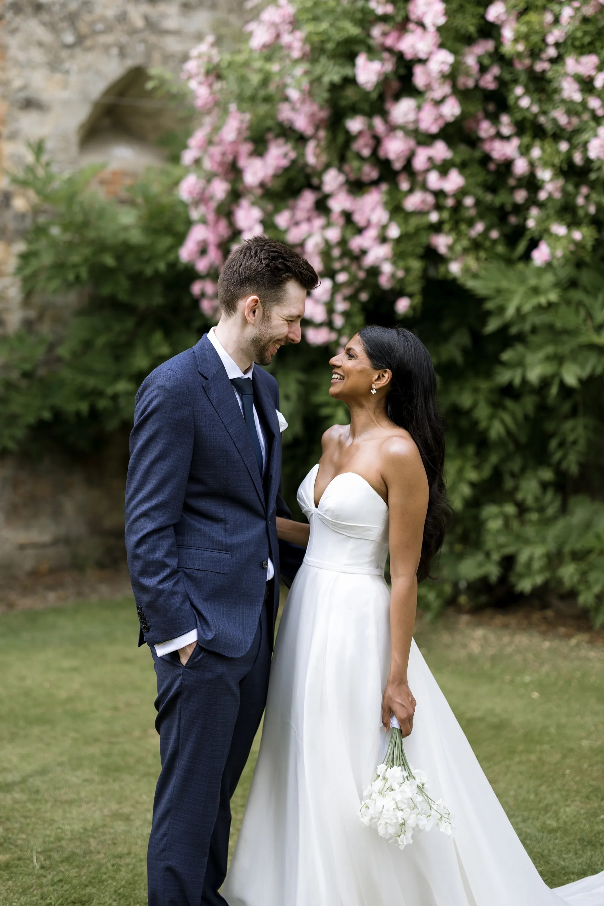 Fusion HIndu Wedding Newburgh Priory 76 - Hema & Will's Fusion Wedding & Hindu Ceremony at Newburgh Priory Bride wears Suzanne Neville and groom wears a navy blue suit. They are looking at one another lovingly.