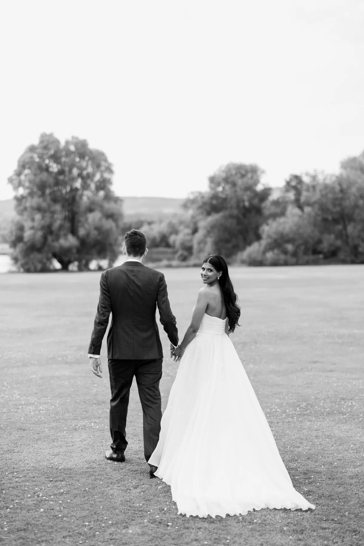 Fusion HIndu Wedding Newburgh Priory 85 - Hema & Will's Fusion Wedding & Hindu Ceremony at Newburgh Priory Black and white over the shoulder shot of a bride in a Suzanne Neville gown as she walks the grounds of Newburgh Priory hand in hand with her groom.