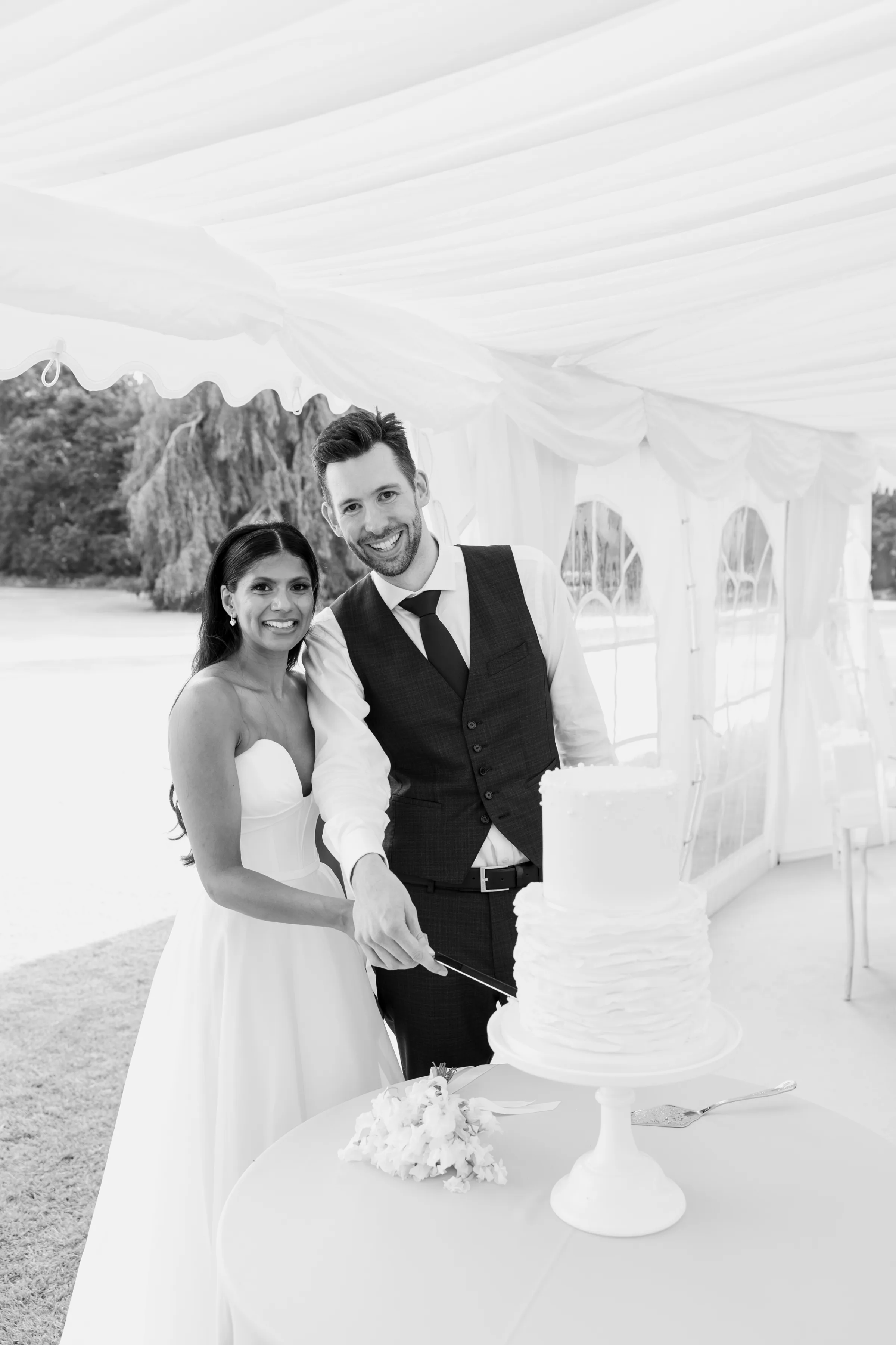 HEMA WILL 91 - Hema & Will's Fusion Wedding & Hindu Ceremony at Newburgh Priory Bride in a Suzanne Neville wedding dress with her groom as they cut the wedding cake inside a white marquee.