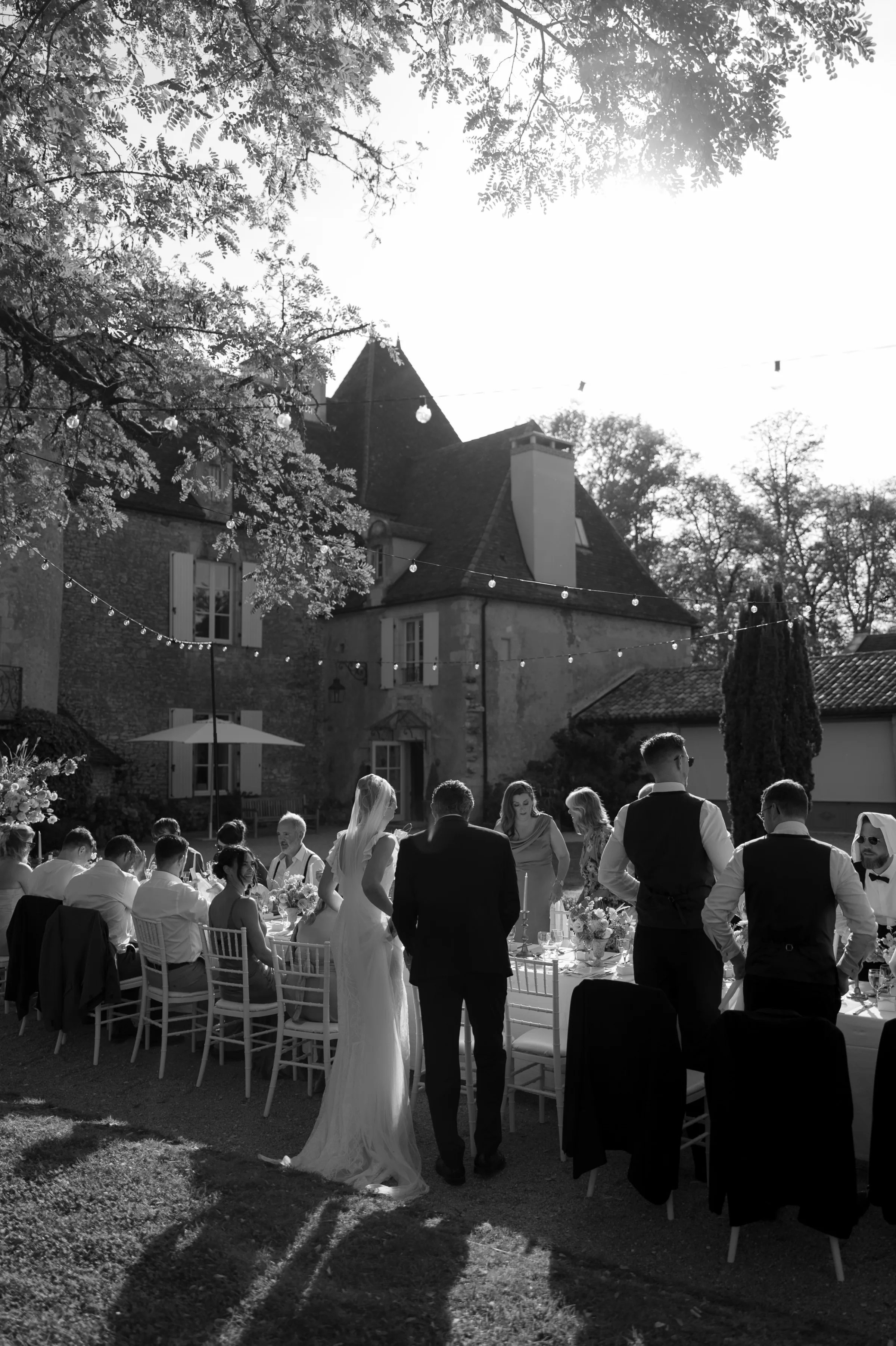 Indie Bride London Chateau Cazenac wedding France 105 - Laura & Ben's Romantic & Intimate Wedding Day Gathering at Chateau Cazenac in The Dordogne Bride and groom arrive for their intimate outdoor wedding reception in the grounds of Chateau Cazenac. A long table with seats either side hosts an outdoor dining experience. Festoon lights hang over head ready to light up the scene when night arrives.