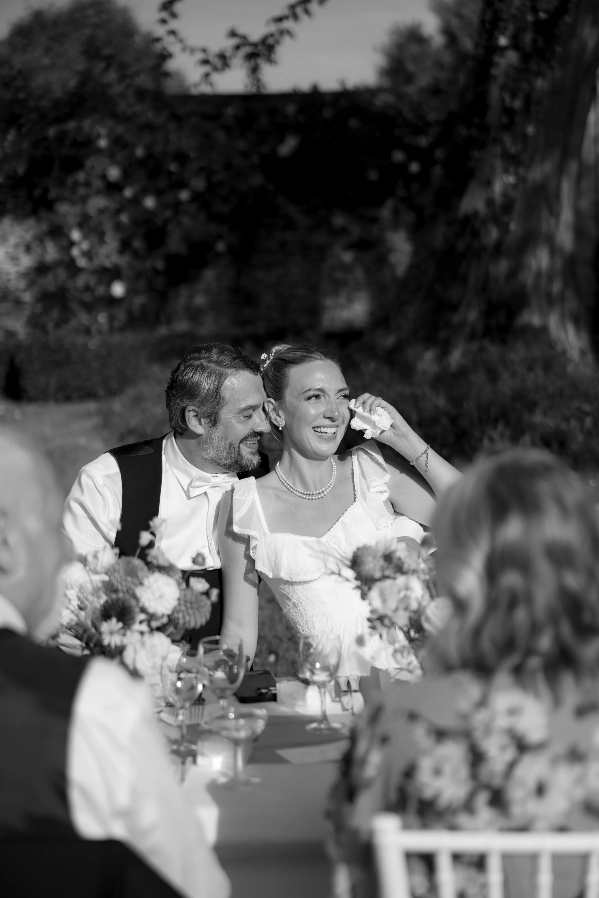 Indie Bride London Chateau Cazenac wedding France 114 - Laura & Ben's Romantic & Intimate Wedding Day Gathering at Chateau Cazenac in The Dordogne Natural wedding photography capturing an intimate and romantic moment between bride and groom during the seated outdoor reception as they smile and laugh.