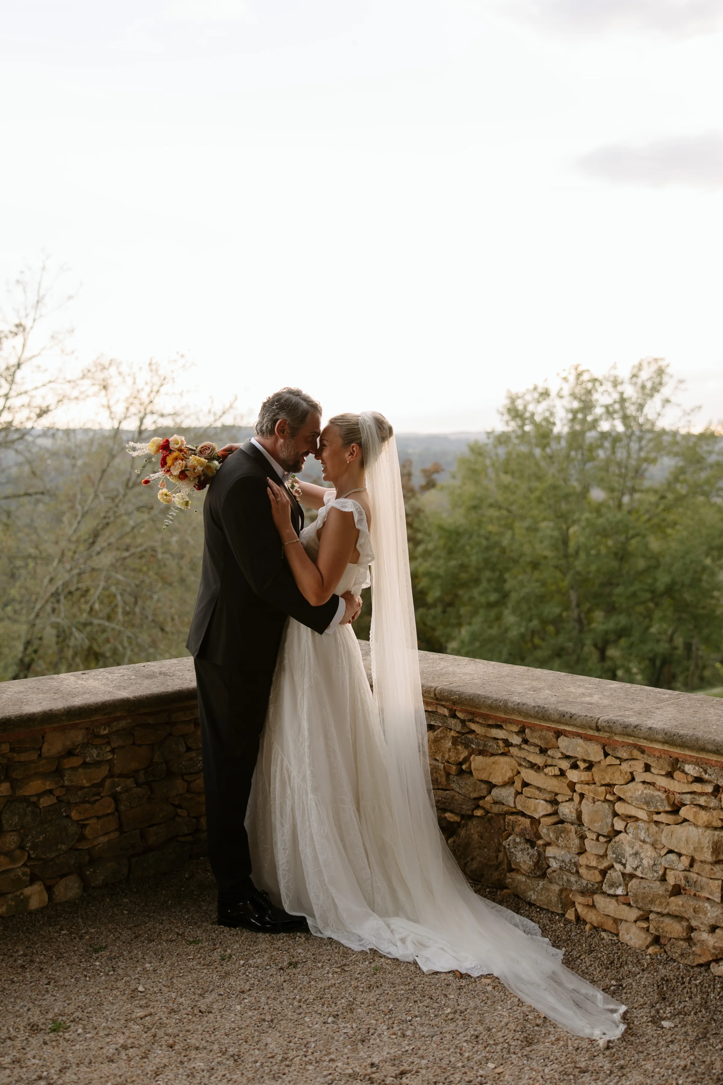 Indie Bride London Chateau Cazenac wedding France 137 - Laura & Ben's Romantic & Intimate Wedding Day Gathering at Chateau Cazenac in The Dordogne Intimate and romantic shot of bride and groom hugging and touching noses on a balcony overlooking trees for their French Chateau wedding.