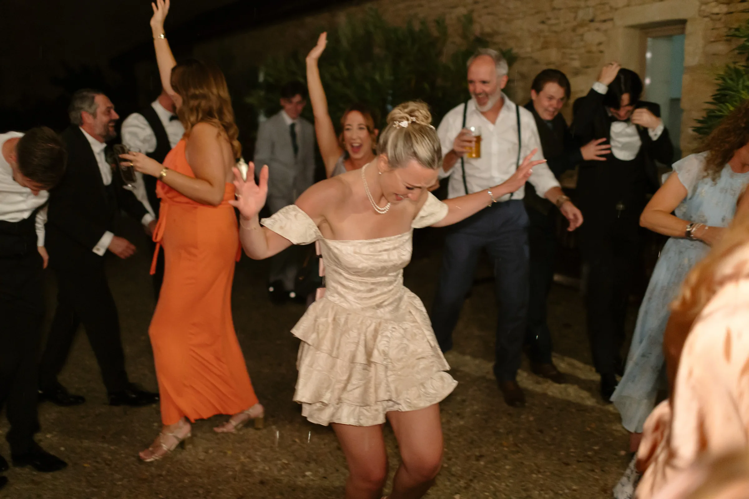 Indie Bride London Chateau Cazenac wedding France 186 - Laura & Ben's Romantic & Intimate Wedding Day Gathering at Chateau Cazenac in The Dordogne Bride in a cute wears a cute tiered mini dress dancing with wild abandon on her wedding day. She has her hair tied up in a tall messy bun and wears a pearl necklace.