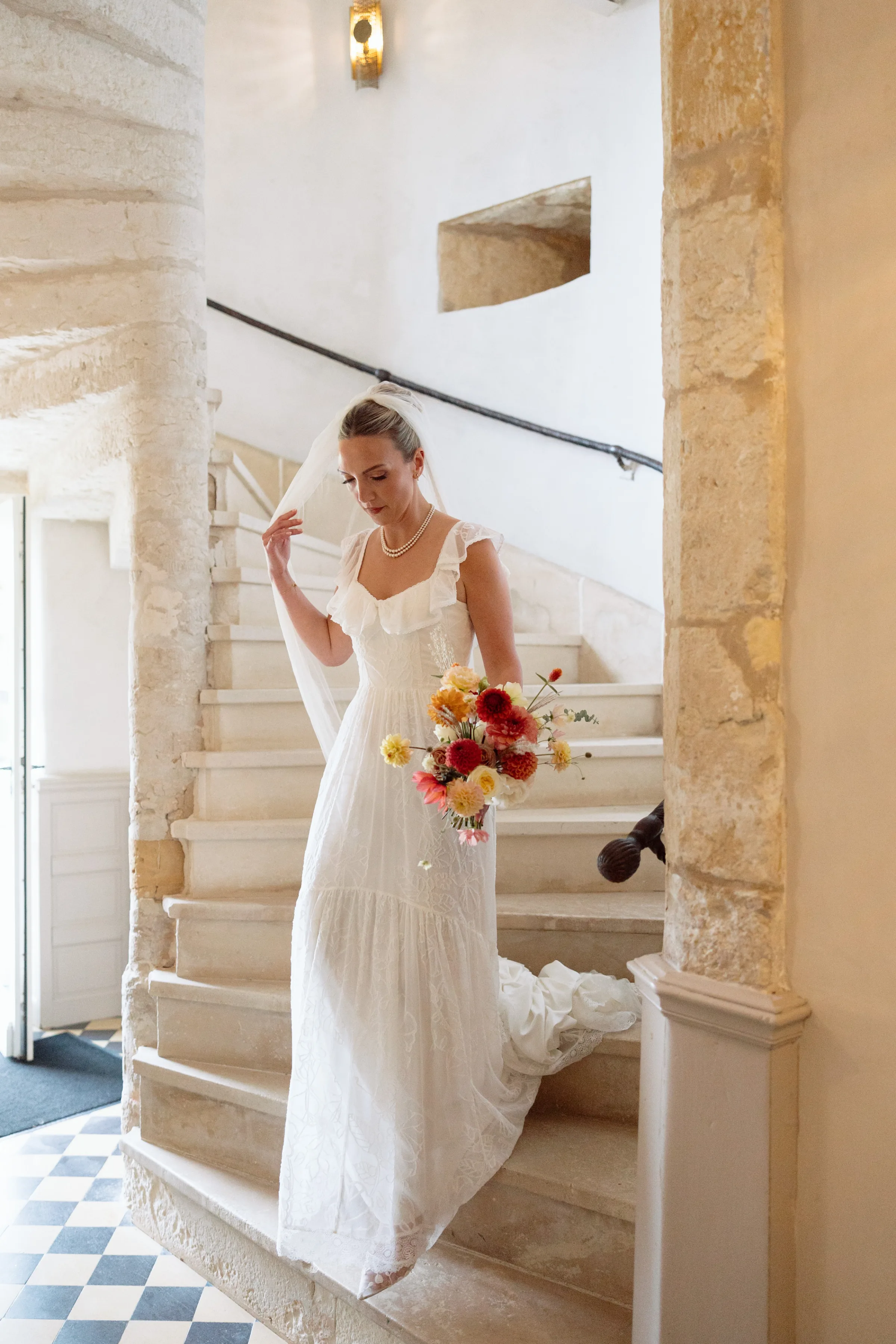 Indie Bride London Chateau Cazenac wedding France 44 - Laura & Ben's Romantic & Intimate Wedding Day Gathering at Chateau Cazenac in The Dordogne Bride making her way down the stairs for the wedding ceremony. She carries a colourful Autumn wedding bouquet.
