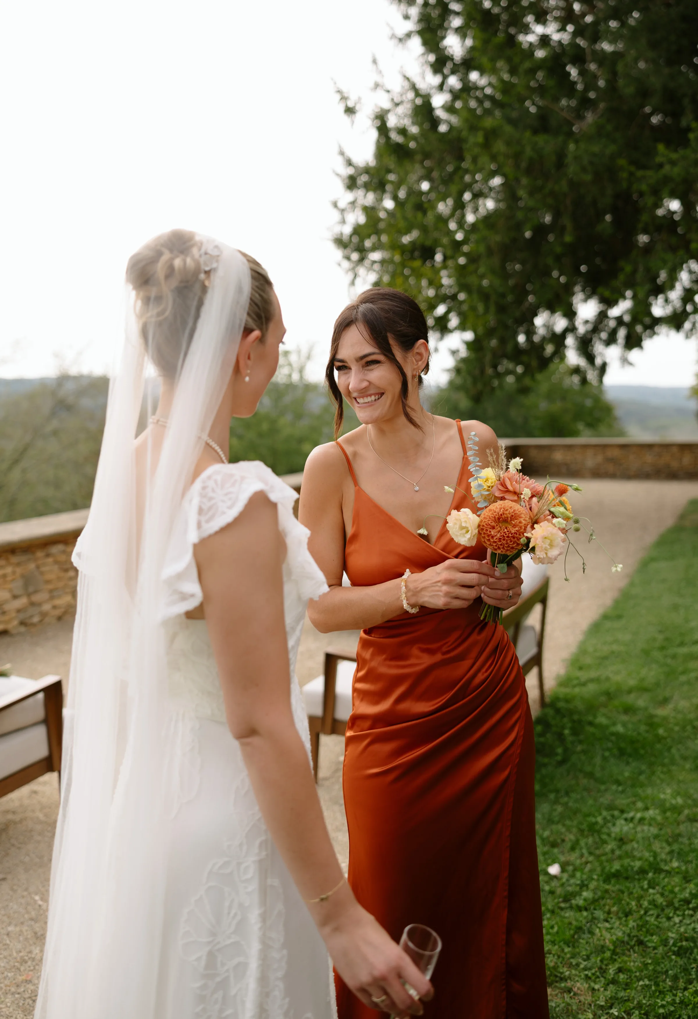 Indie Bride London Chateau Cazenac wedding France 73 - Laura & Ben's Romantic & Intimate Wedding Day Gathering at Chateau Cazenac in The Dordogne Bride looking towards her bridesmaid wearing a burnt orange dress and carrying a bouquet with burnt orange flowers.