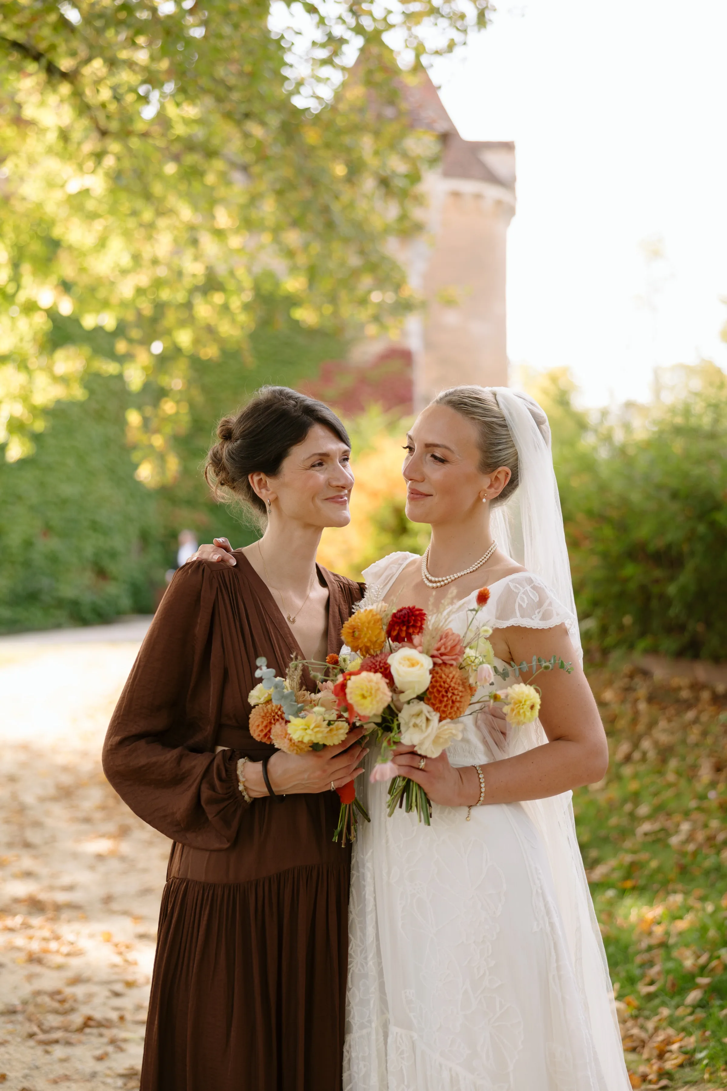Indie Bride London Chateau Cazenac wedding France 94 1 - Laura & Ben's Romantic & Intimate Wedding Day Gathering at Chateau Cazenac in The Dordogne Portrait of a bride and her bridesmaid both carrying colourful Autumn wedding bouquets. The bridesmaid wears brown silken the bride wears a simple dress with ruffle detail around the neck and her blonde hair up in a high bun.
