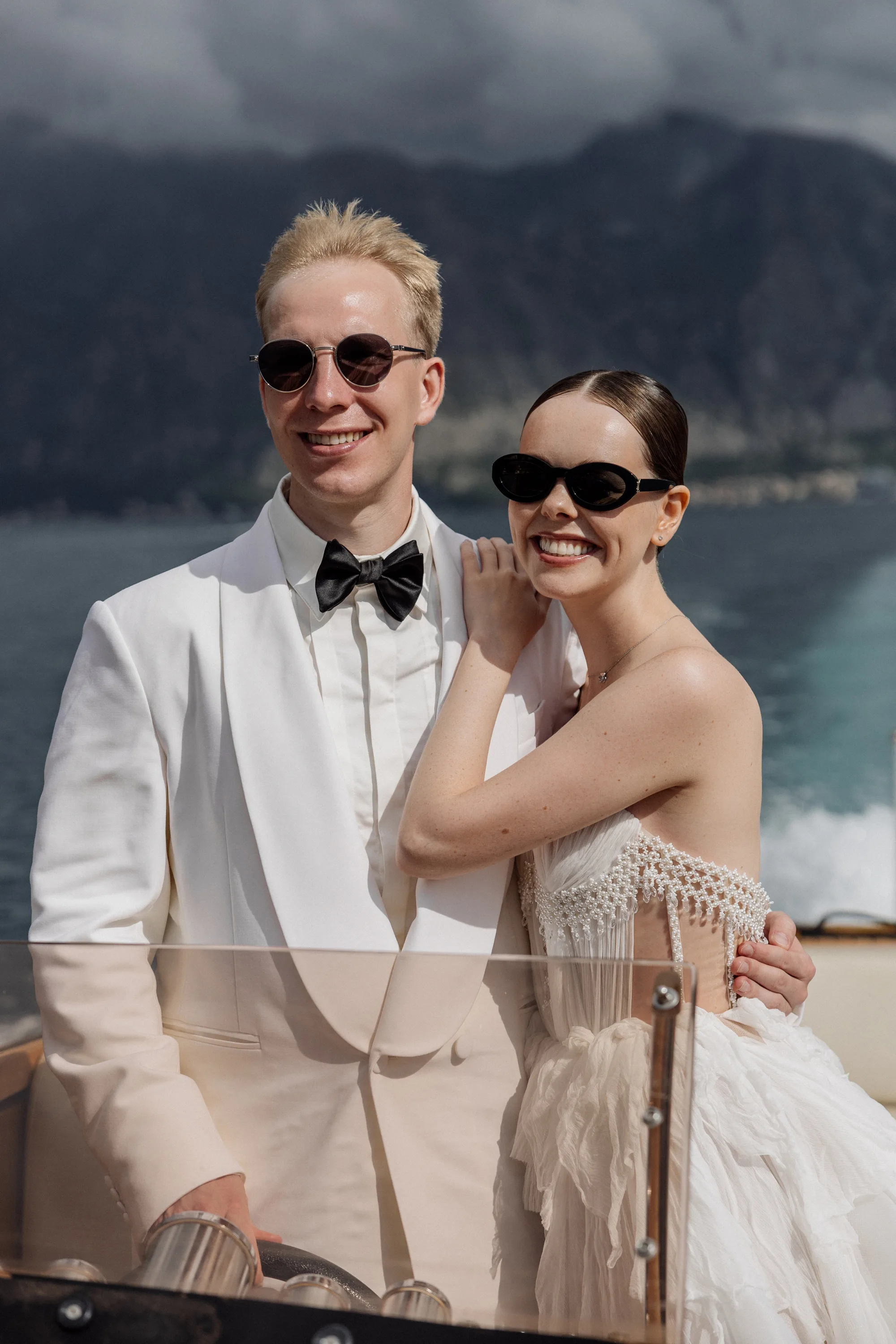 Montenegro Wedding 37 - A Romantic & Intimate Montenegro Wedding at Villa Shah, Inspired by 'La Vita Nobile' Portraits of a bride and groom on a speedboat in Montenegro. Groom wears a white tuxedo jacket and black bow tie. The bride wears a Rara Couture gown with compressed silk corset detail. They both wear sunglasses.