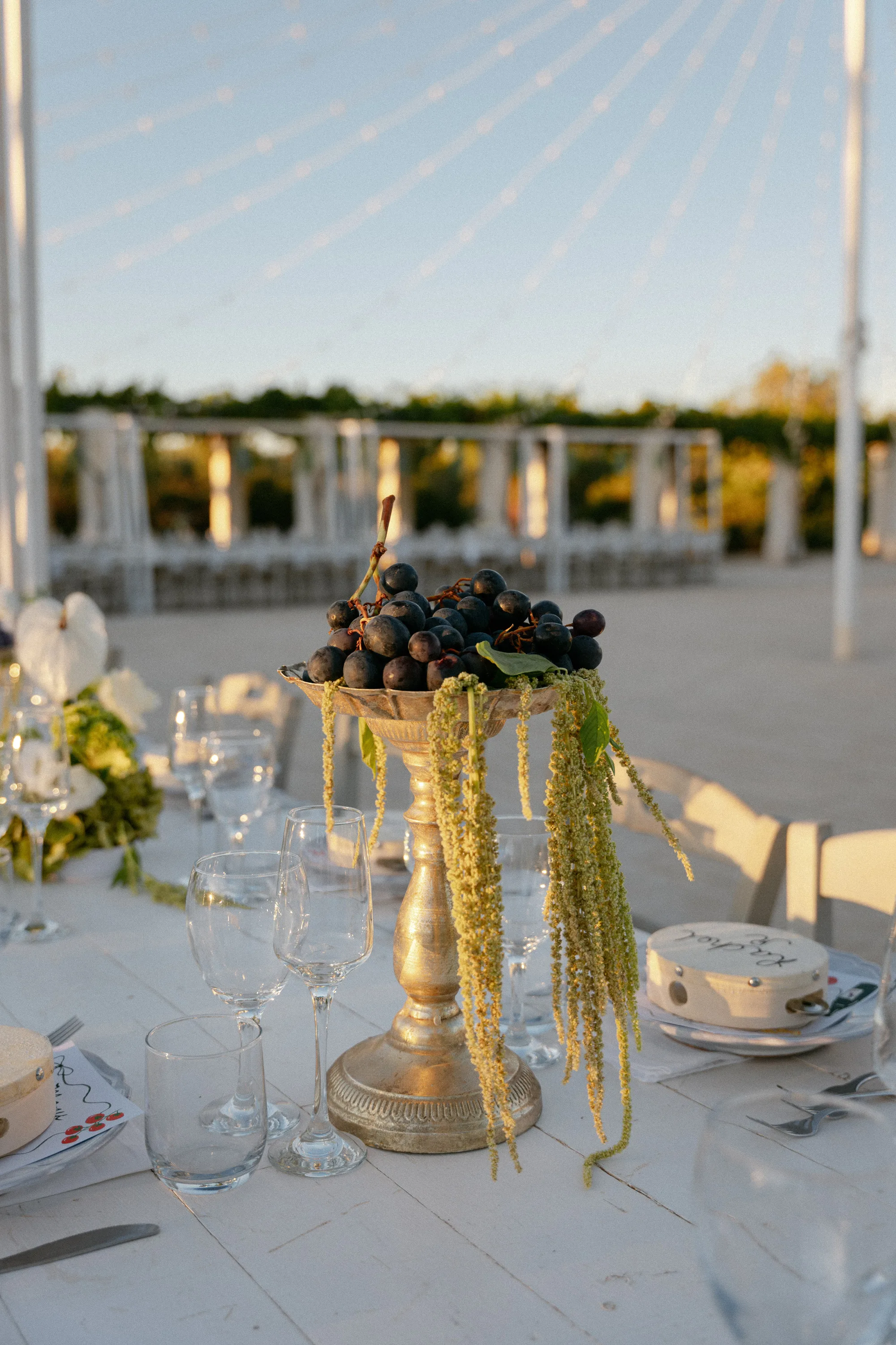 Multiple Day Destination Wedding in Masseria Potenti Puglia Italy 114 - Yael Wore Chana Marelus & A Handmade Beaded Veil for her Relaxed Italian Masseria Wedding Tall brass stand holding grapes and training greenery. A tambourine sits on top of a plate serving as a guest favour.