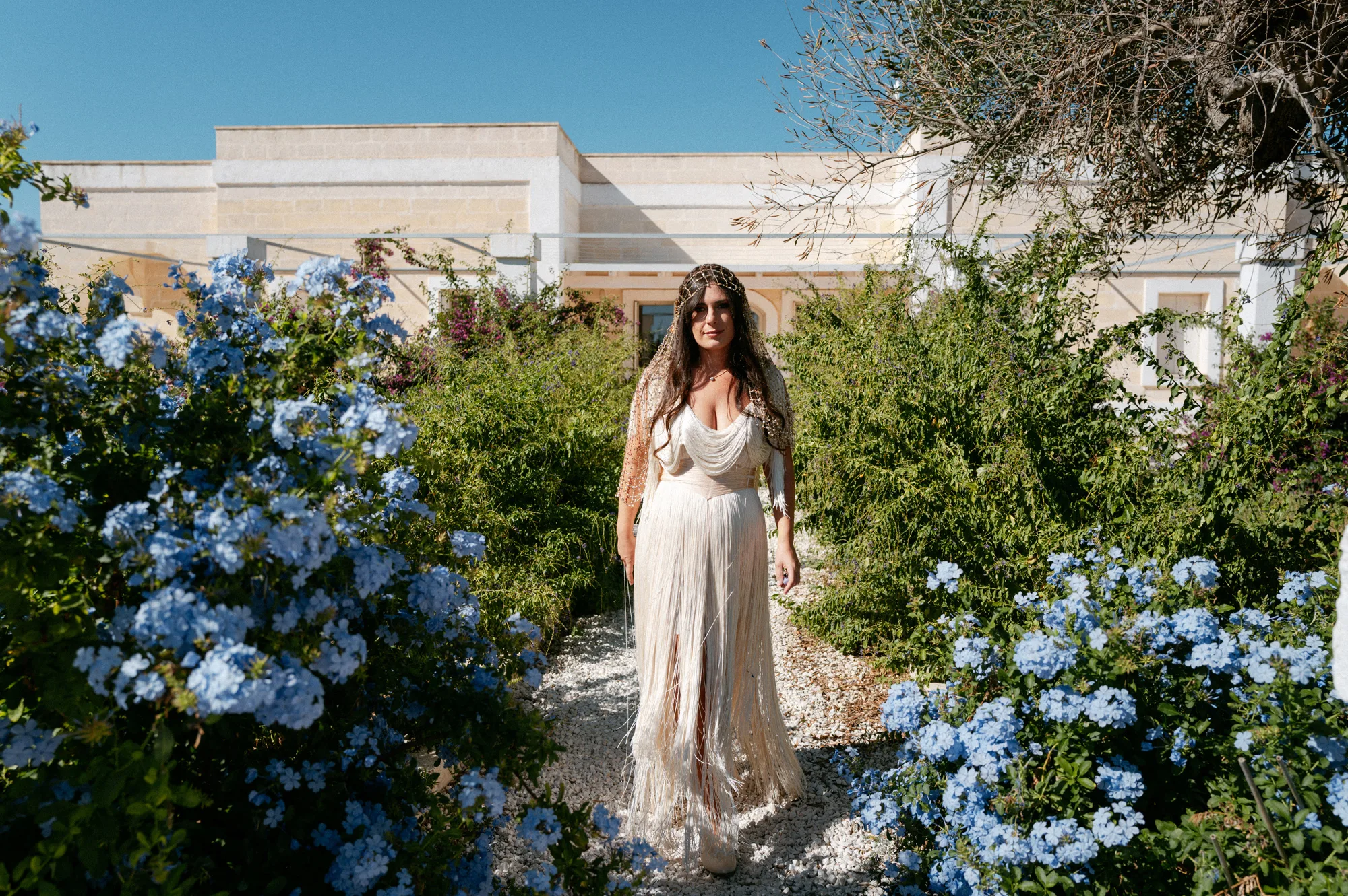 Multiple Day Destination Wedding in Masseria Potenti Puglia Italy 29 1 - Yael Wore Chana Marelus & A Handmade Beaded Veil for her Relaxed Italian Masseria Wedding Bride wearing a Chana Marelus with tassels and a beaded veil, standing in the gardens of her Italian wedding villa in Puglia.