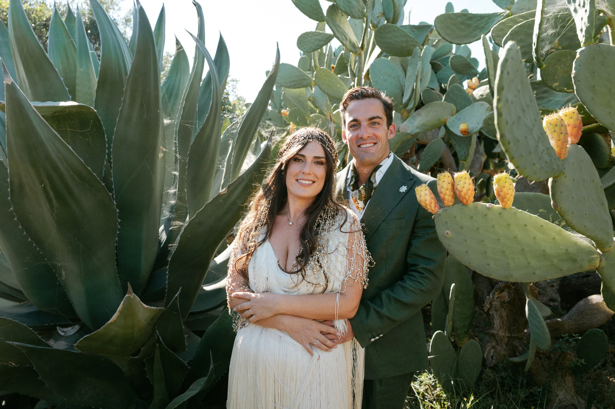 Multiple Day Destination Wedding in Masseria Potenti Puglia Italy 36 - Yael Wore Chana Marelus & A Handmade Beaded Veil for her Relaxed Italian Masseria Wedding Bride wearing a Chana Marelus with tassels and a beaded veil being embraced by her groom in. a green linen suit in the grounds of their Italian wedding venue.