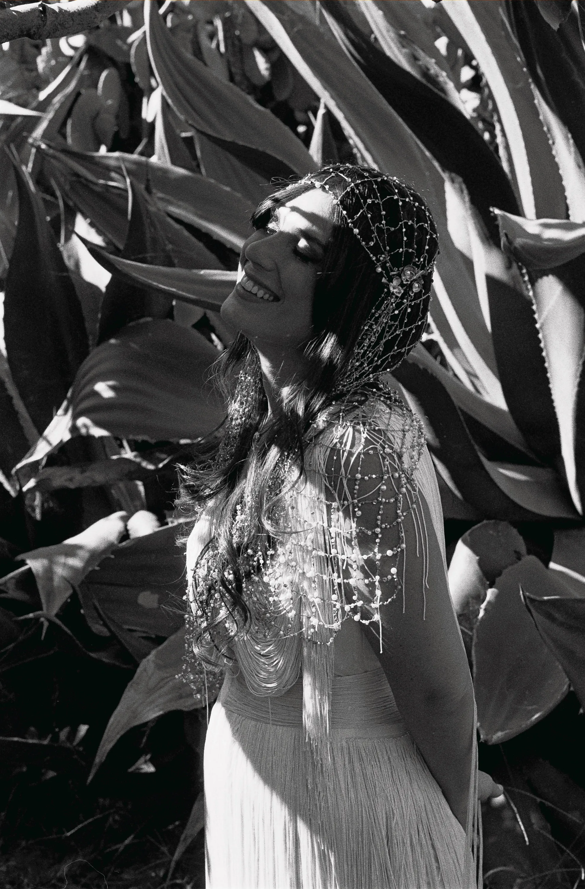 Multiple Day Destination Wedding in Masseria Potenti Puglia Italy 41 1 - Yael Wore Chana Marelus & A Handmade Beaded Veil for her Relaxed Italian Masseria Wedding Black and white photograph of a bride wearing a Chana Marelus tassel dress and beaded veil. She is standing next to large cactus plants.