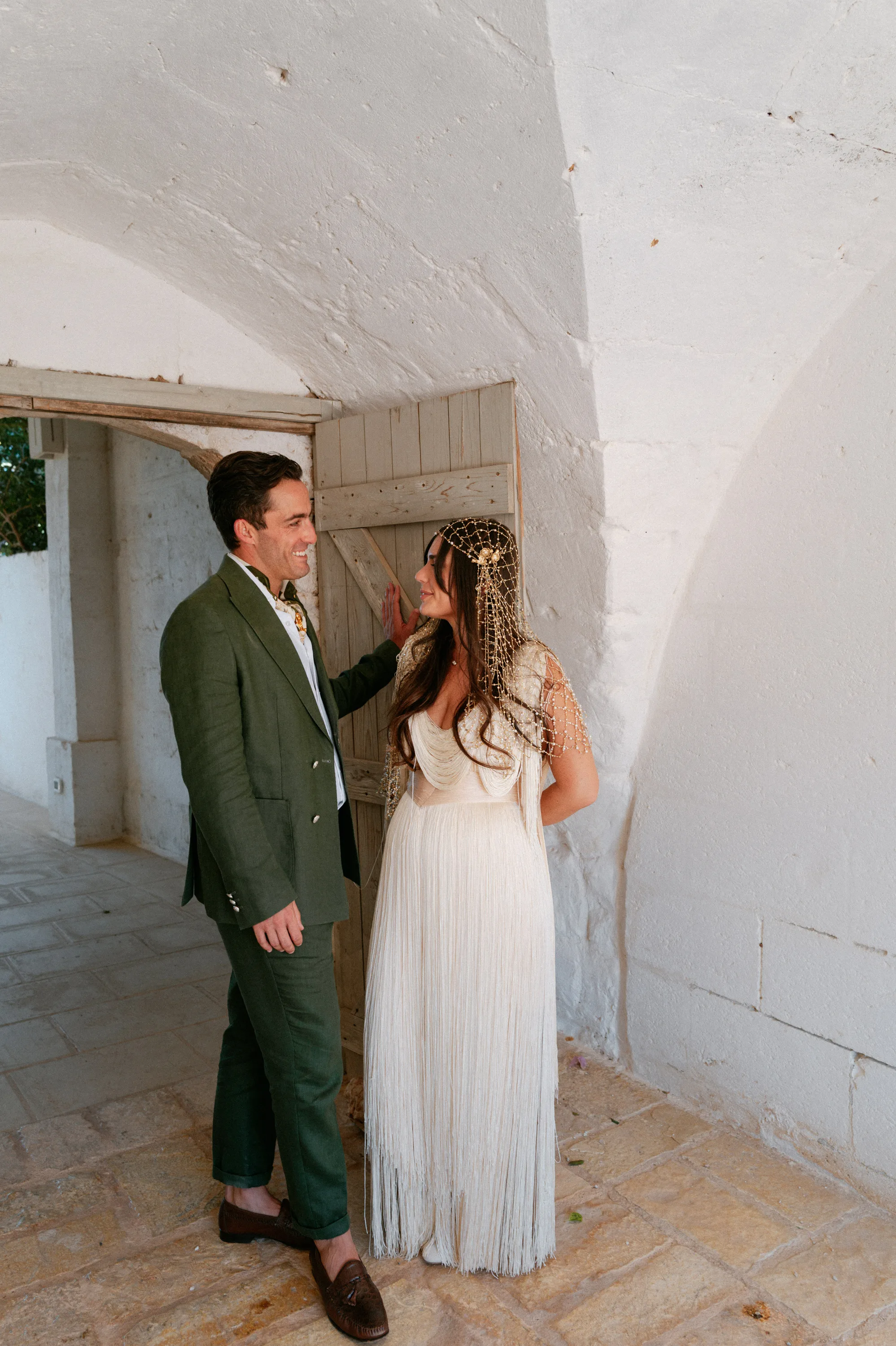 Multiple Day Destination Wedding in Masseria Potenti Puglia Italy 45 1 - Yael Wore Chana Marelus & A Handmade Beaded Veil for her Relaxed Italian Masseria Wedding Bride wearing a Chana Marelus tassel dress and beaded veil standing by her groom who is wearing a green linen suit and cravat.