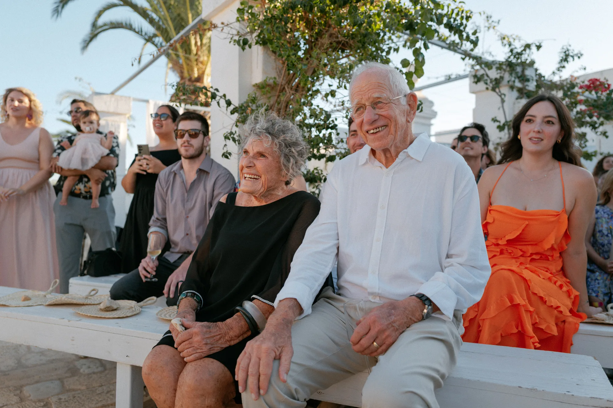 Multiple Day Destination Wedding in Masseria Potenti Puglia Italy 72 - Yael Wore Chana Marelus & A Handmade Beaded Veil for her Relaxed Italian Masseria Wedding Seated, elderly wedding guests smiling and laughing during an outdoor wedding ceremony in Puglia, Italy.