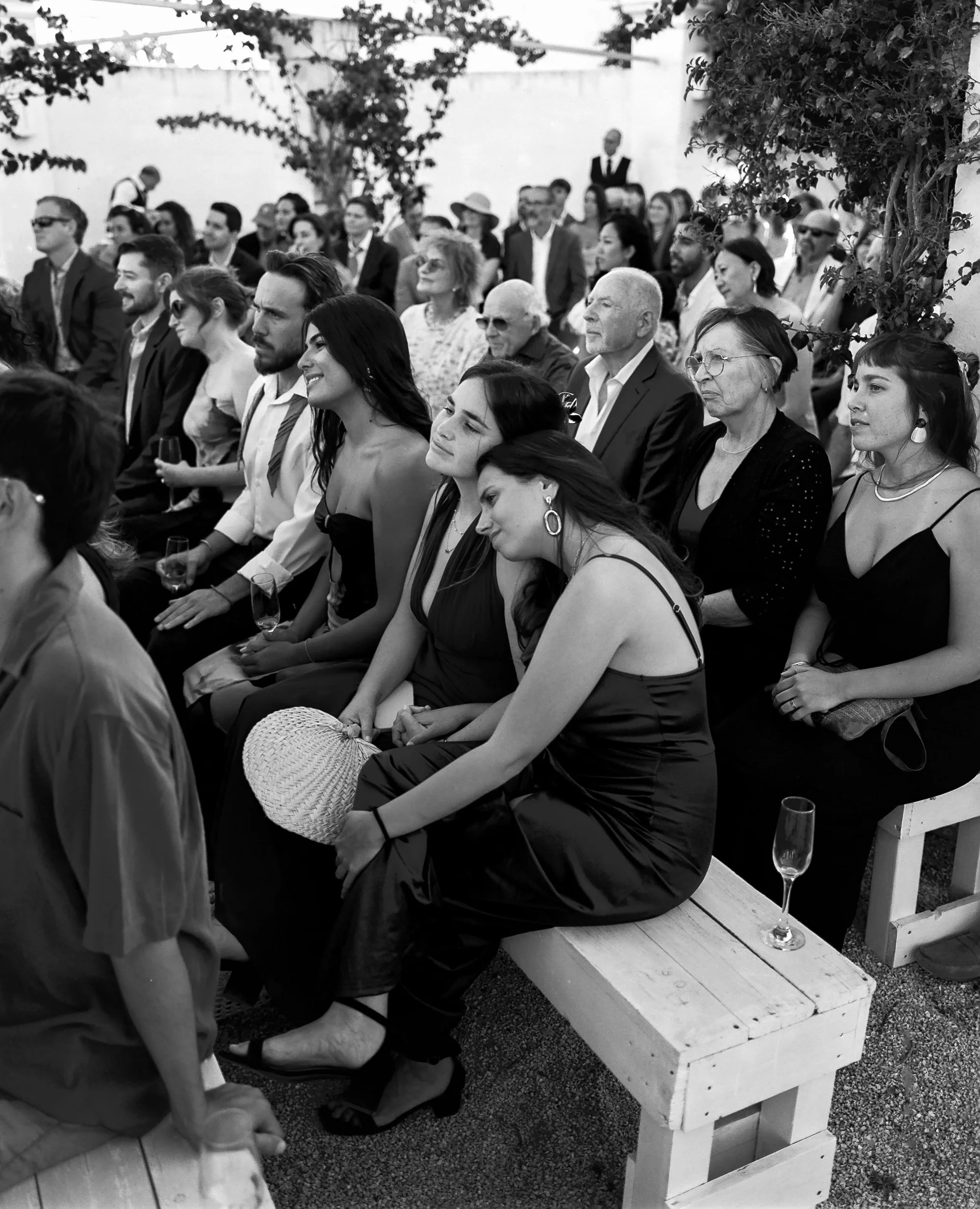 Multiple Day Destination Wedding in Masseria Potenti Puglia Italy 77 - Yael Wore Chana Marelus & A Handmade Beaded Veil for her Relaxed Italian Masseria Wedding Black and white photography of a female wedding guest tenderly leaning into the shoulder of another wedding guests as they witness a wedding ceremony.