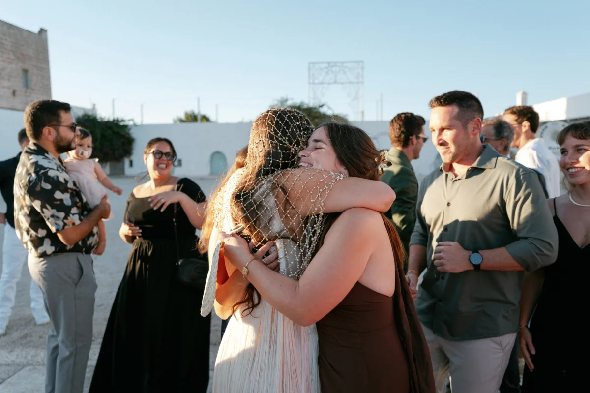 Multiple Day Destination Wedding in Masseria Potenti Puglia Italy 91 - Yael Wore Chana Marelus & A Handmade Beaded Veil for her Relaxed Italian Masseria Wedding Bride in a beaded wedding veil being hugged tightly by a happy wedding guest. Puglia Italy wedding.
