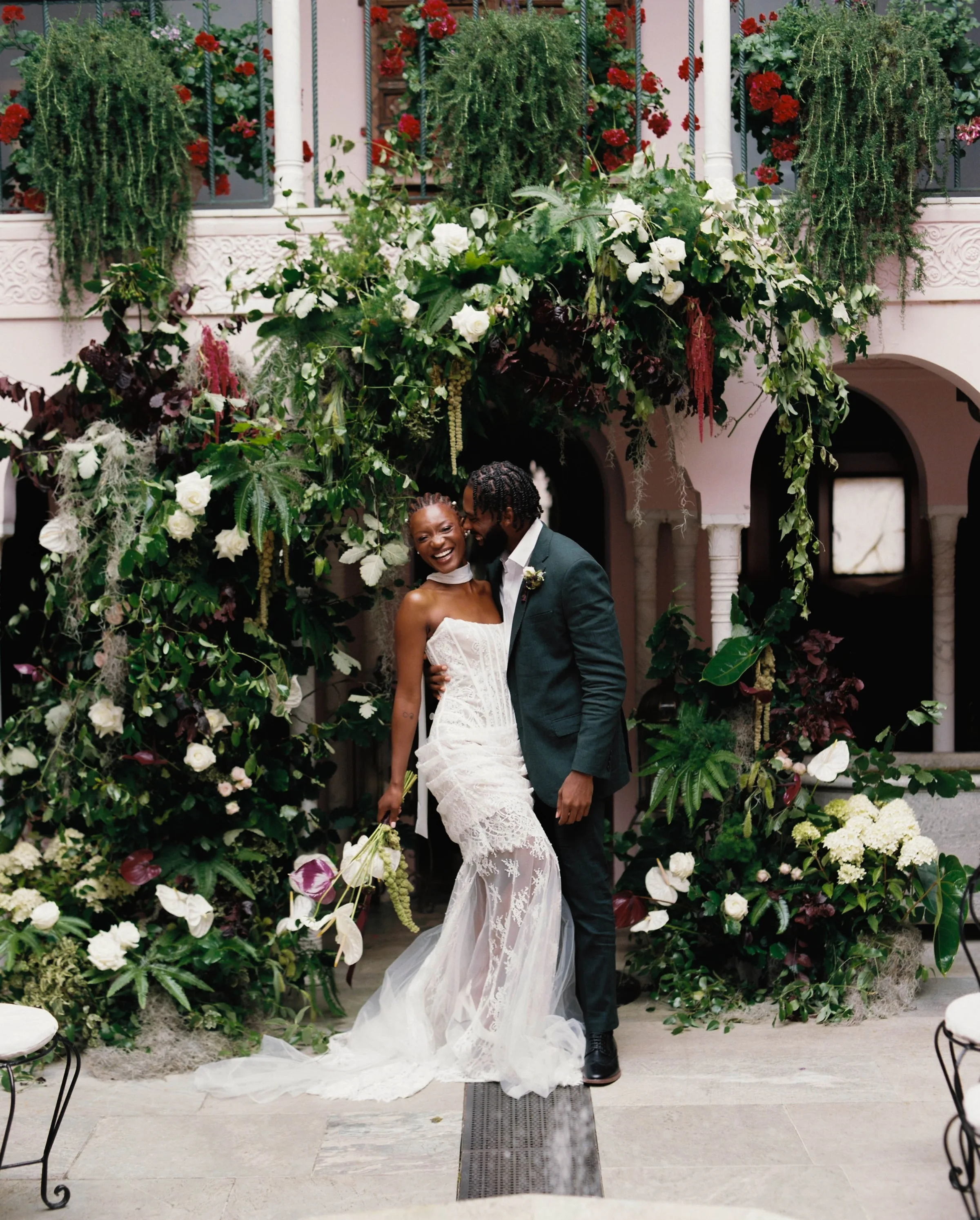 Port Lympne Safari Park New Orleans Wedding Editorial The Chamberlins Film Medium Format Photography London Surrey 70 - Wedding Inspiration That Celebrates The Joy, Diversity & Vibrancy of New Orleans Black model bride and groom embracing beside a palm plant at Port Lympne Resort in Kent. Scene inspired by New Orleans. The bride wears pearls in her braided hair.