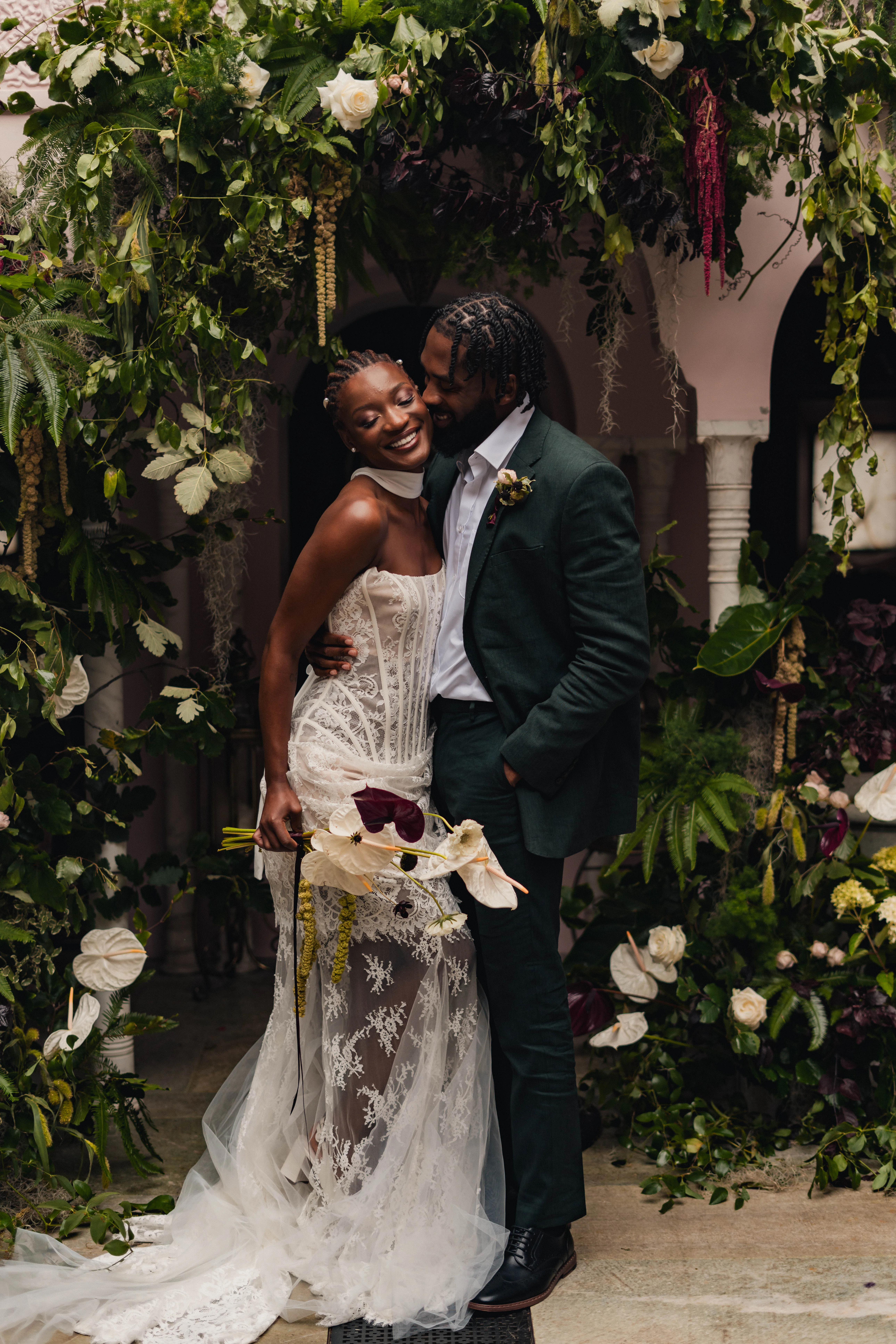 SS Port Lympne Safari Park New Orleans Wedding Editorial The Chamberlins Film Medium Format Photography London Surrey 299 - Wedding Inspiration That Celebrates The Joy, Diversity & Vibrancy of New Orleans Black model bride and groom embracing beside a palm plant at Port Lympne Resort in Kent. Scene inspired by New Orleans. The bride wears pearls in her braided hair.
