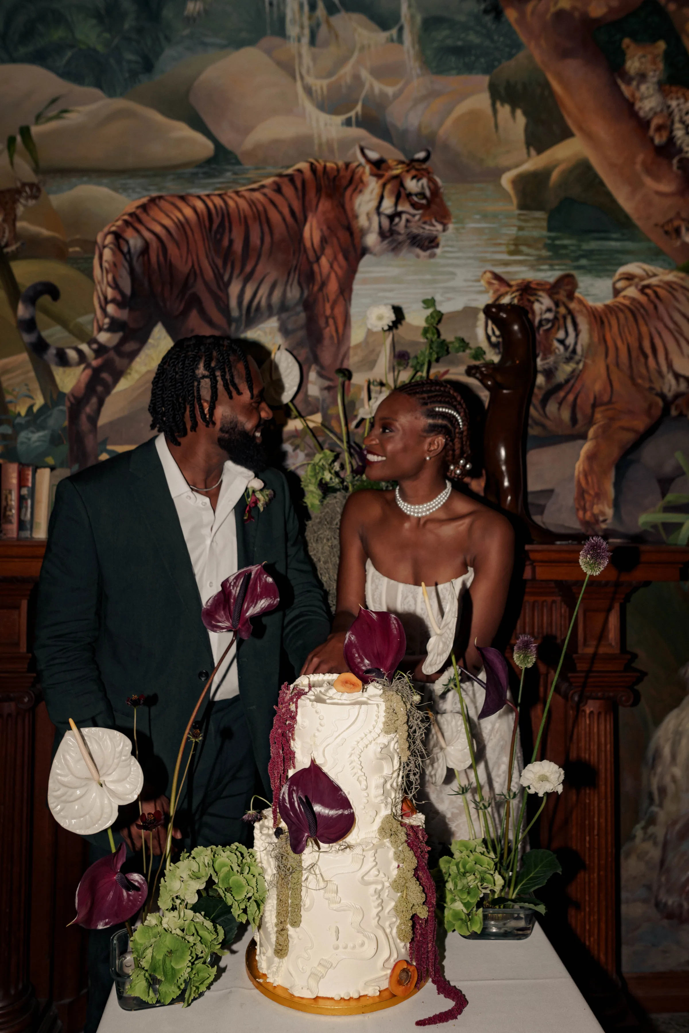 SS Port Lympne Safari Park New Orleans Wedding Editorial The Chamberlins Film Medium Format Photography London Surrey 741 - Wedding Inspiration That Celebrates The Joy, Diversity & Vibrancy of New Orleans Black bride and groom standing by a two tier cake decorated with dark orchids. New Orleans and Mardi Gras inspired wedding editorial at Port Lympne Resort & wedding venue in Kent.