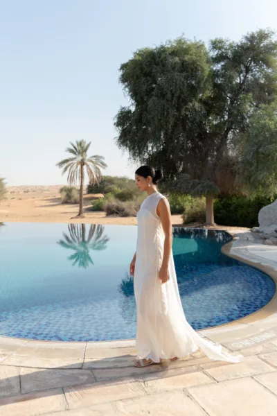 Bride in white walking beside the resort pool framed by palm trees at Al Maha Resort, a Dubai desert wedding