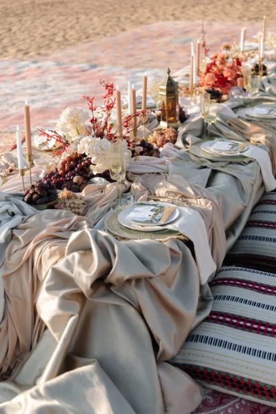 Desert wedding reception table at dusk with candles, autumnal florals and rugs at Al Maha Resort, Dubai, design by Zahra Studio Events