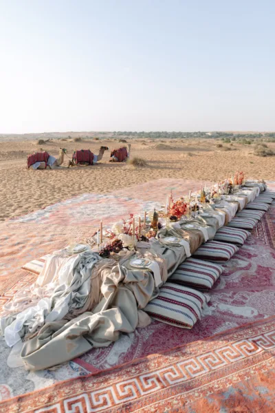 Low desert banquet table with cushions and camels in the distance at Al Maha Resort, Dubai, design by Zahra Studio Events