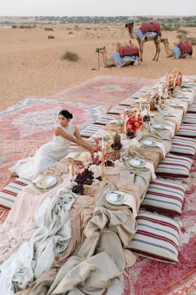 Low desert picnic reception table with rugs and cushions and camels beyond at Al Maha Resort, Dubai, design by Zahra Studio Events