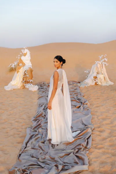 Bride in a flowing grey-blue gown walking through the desert with floral installations at Al Maha Resort, Dubai