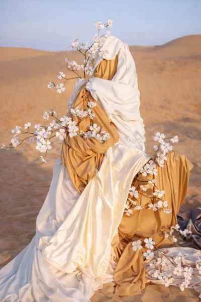 Editorial figure draped in gold fabric adorned with blossom branches in the Dubai desert, styling by Zahra Studio Events
