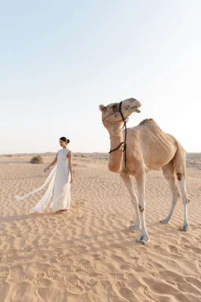 Figure in a white gown with a camel among the dunes at Al Maha Resort, a Dubai desert wedding editorial