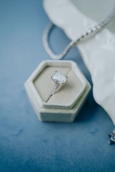 Wedding and engagement rings in a hexagonal velvet ring box on dusty-blue fabric, a wedding detail