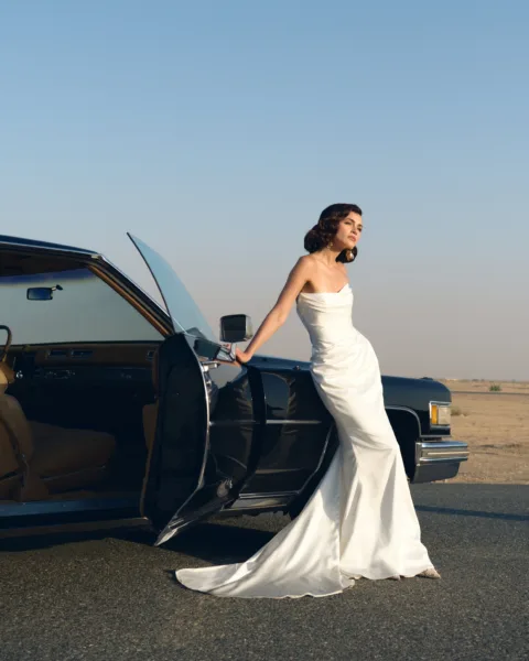 Bride in a white gown stepping from a black classic car in the desert at dusk during a destination wedding