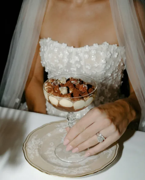 Bride in a floral-applique gown and veil holding a dessert glass at an elegant wedding table