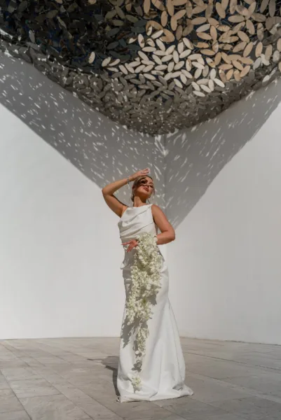 Bride in a sequined gown standing beneath a patterned pergola casting intricate shadows at a destination wedding