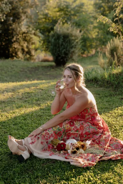 Bride relaxing on the grass in a red floral-print gown at a Tuscan villa wedding