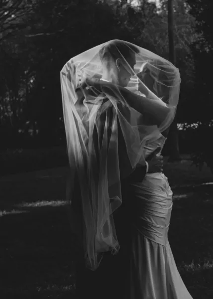 Bride and groom kissing beneath her veil in a dramatic black-and-white 35mm wedding portrait