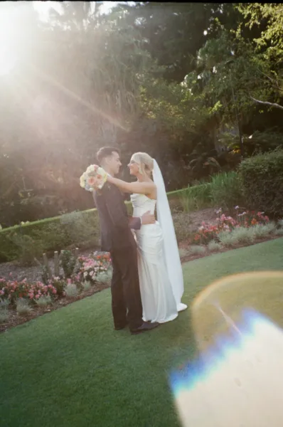 Bride and groom kissing in a garden at golden hour, captured with soft lens flare on 35mm wedding film.