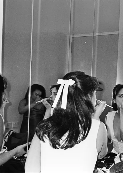 Bridesmaids getting ready together, with one wearing a white ribbon in her hair, photographed in black and white.