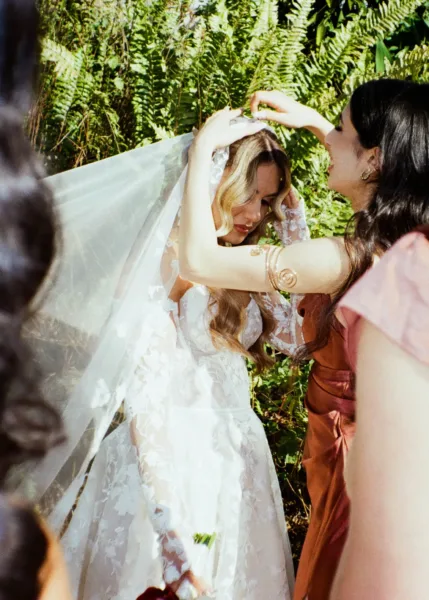 Bridesmaid adjusting the bride’s lace veil outdoors in a candid documentary-style wedding photograph by The Light Photo & Film.