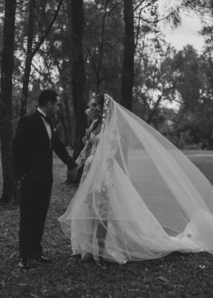 Bride and groom holding hands beneath her long veil in a romantic black-and-white wedding portrait.