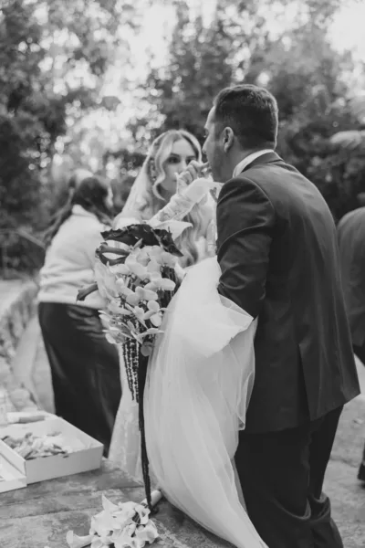 Groom carrying the bride after their outdoor wedding ceremony, captured in candid black-and-white film photography.