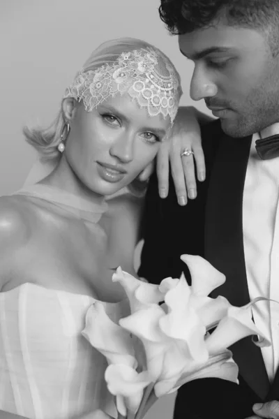 Intimate portrait of a couple embracing, the bride wearing a jeweled headpiece and holding a white calla lily