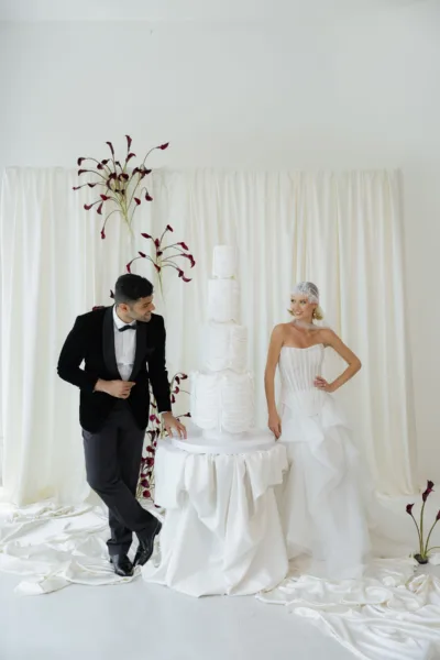 Newlyweds beside a white tiered wedding cake with dark branch decor, luxury wedding design by Zahra Studio Events