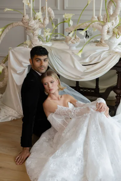 Bride in a white lace ballgown and groom seated within an elegant draped white wedding setting designed by Zahra Studio Events