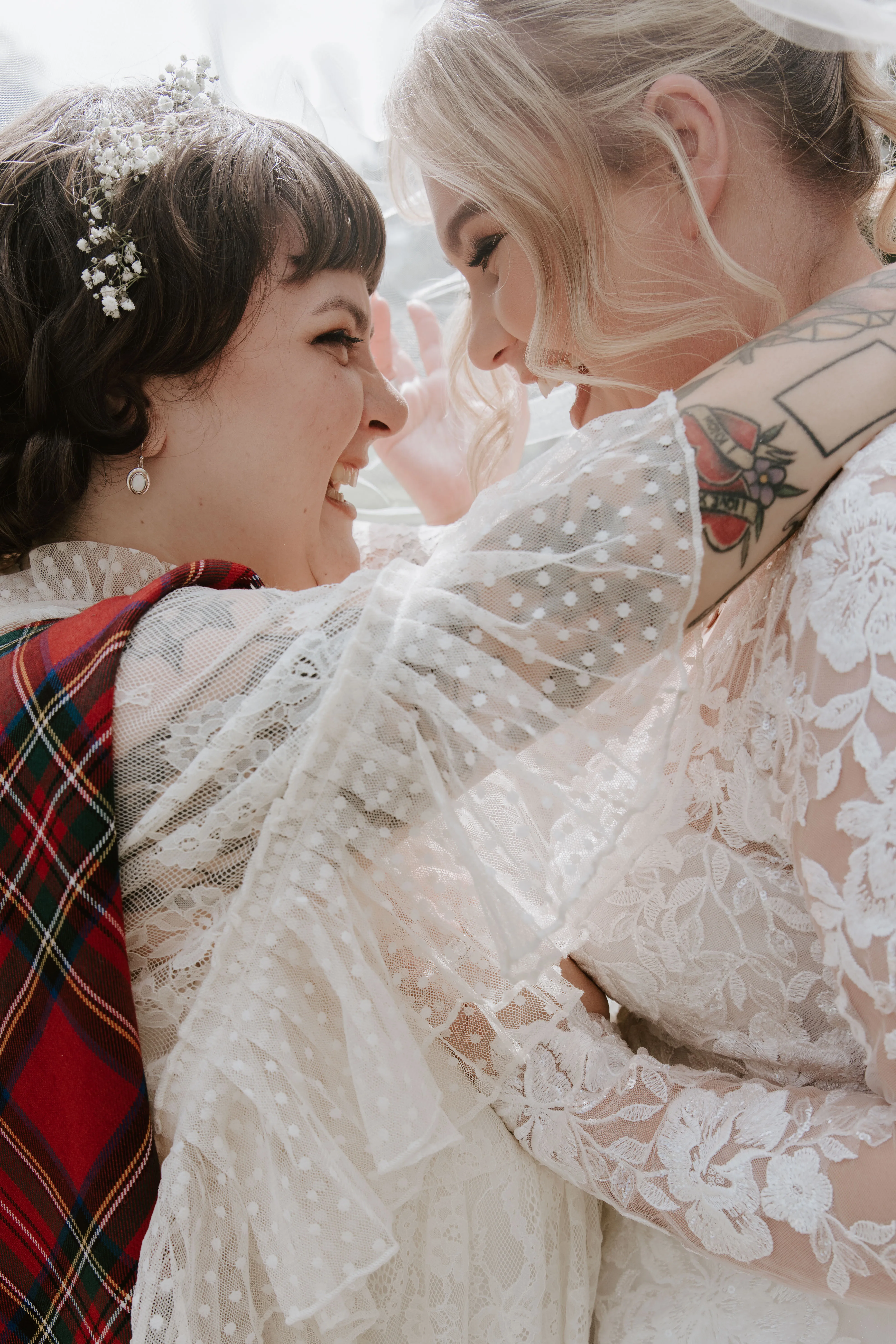 two young woman smile and laugh in wedding dresses under a veil
