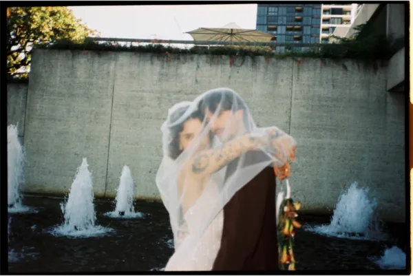 Bride and groom kissing beneath her veil beside a modern water feature, captured on 35mm wedding film.